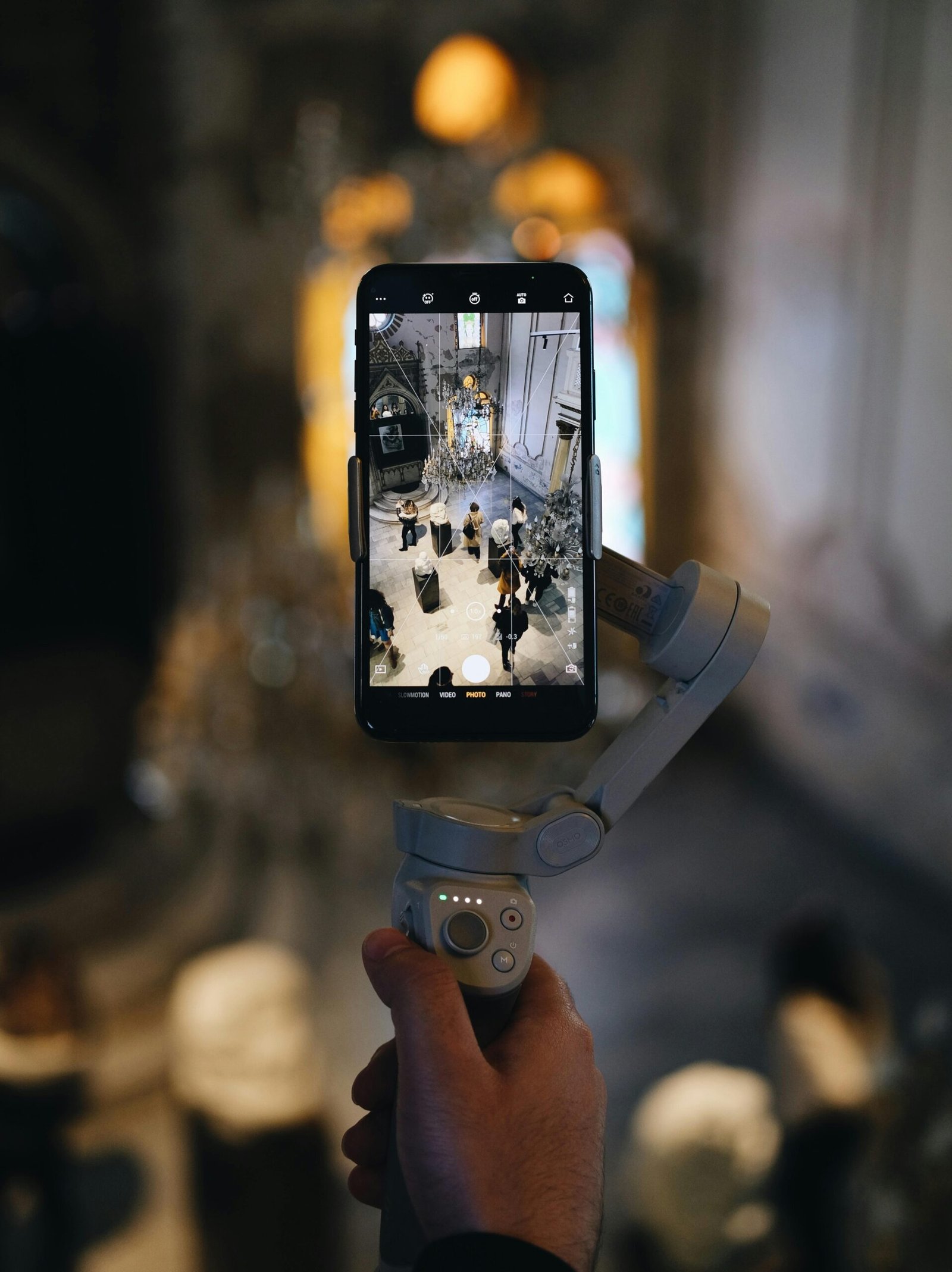 Hand holding a smartphone on a gimbal, capturing a grand interior scene.